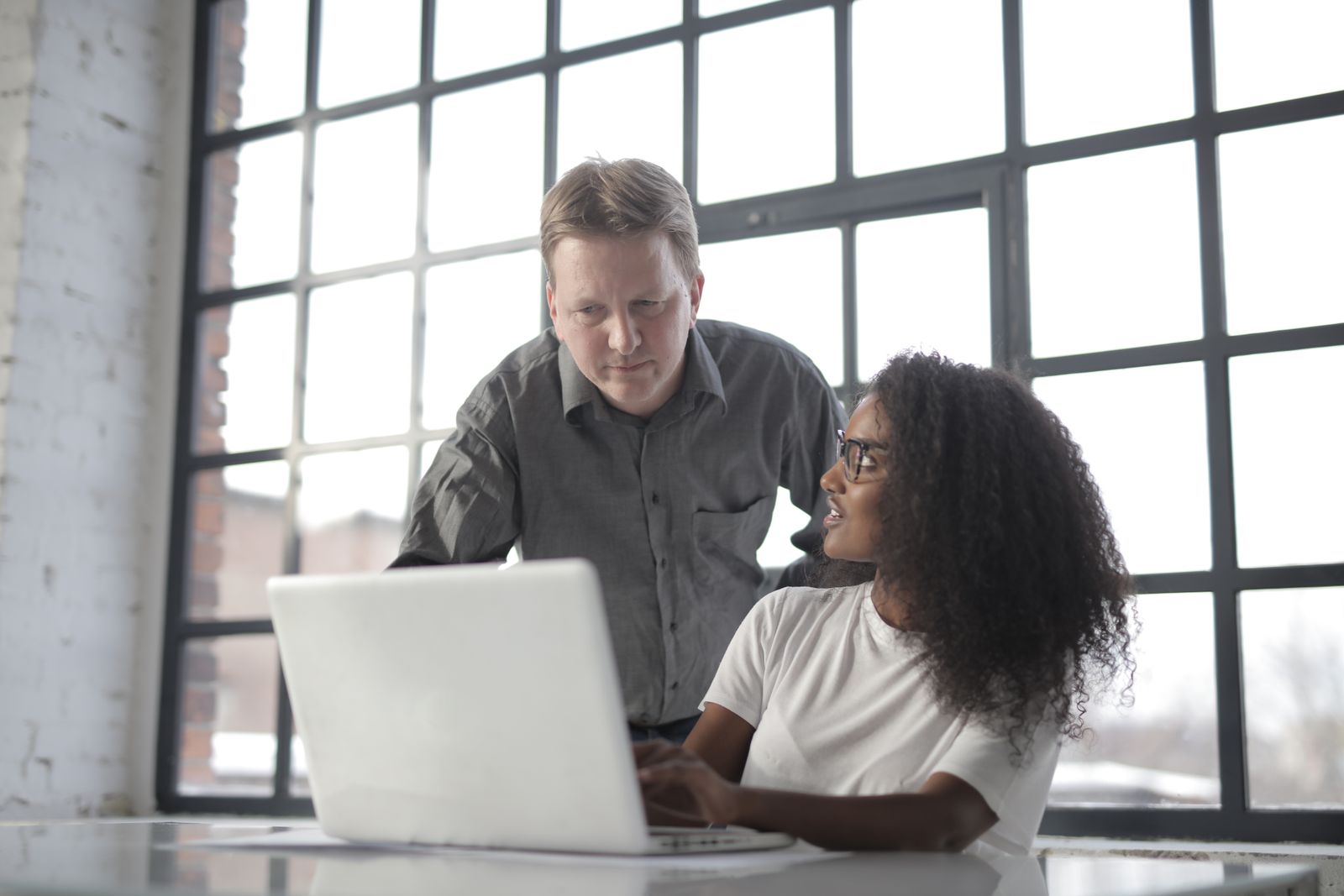 An adviser and a student looking at a laptop together by a large window