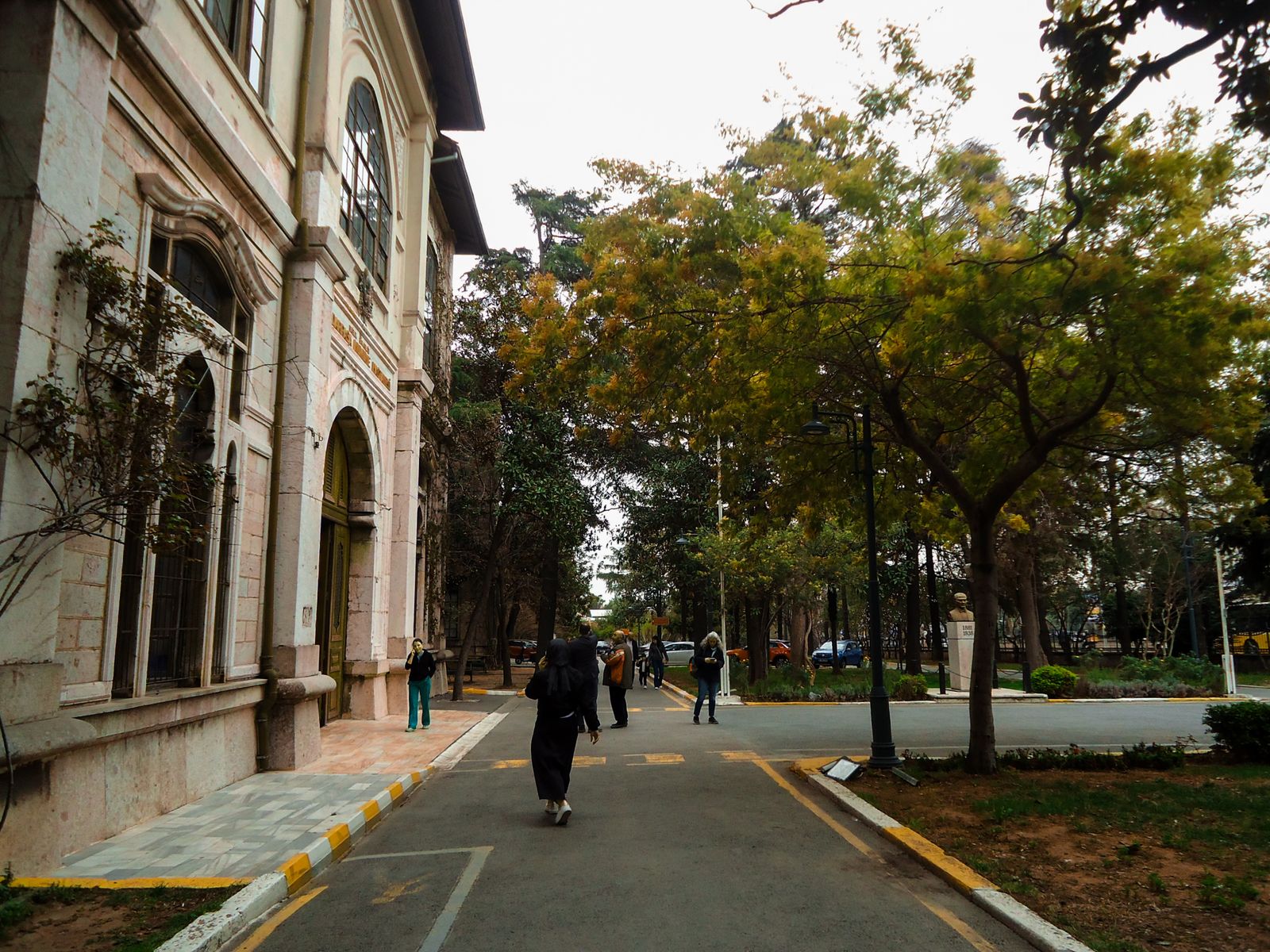People walking along a tree-lined path past old university buildings