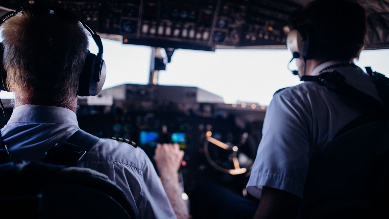 Two pilots in the cockpit seen from behind, headsets on