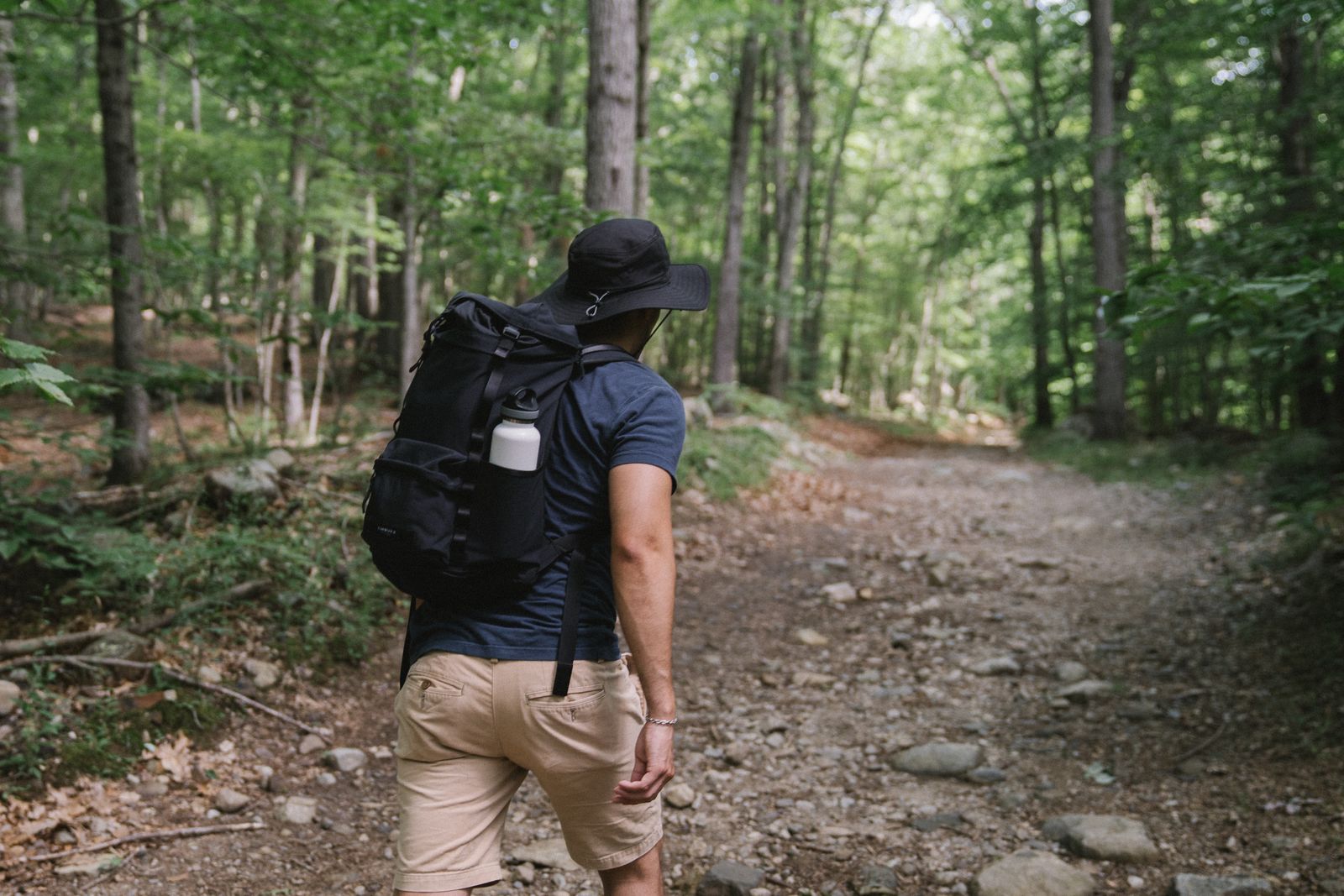 A walker with a backpack and a hat on a dirt path through a green forest