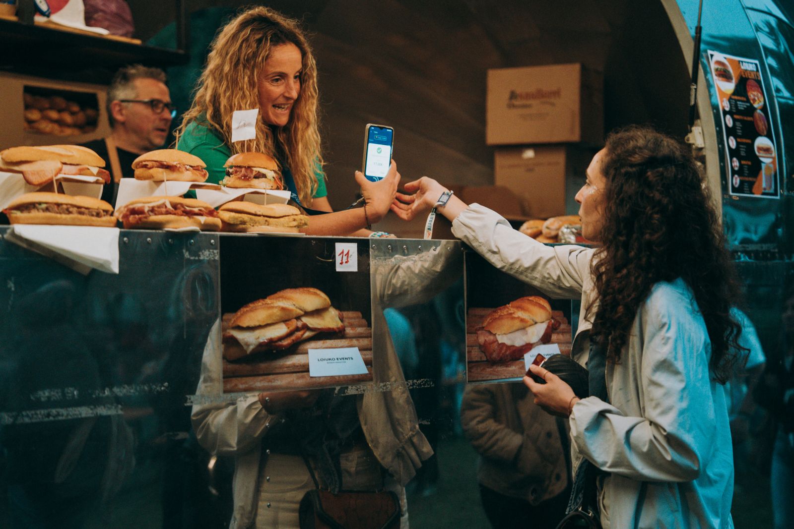 A customer paying with her phone at a sandwich food truck, the seller holding the terminal