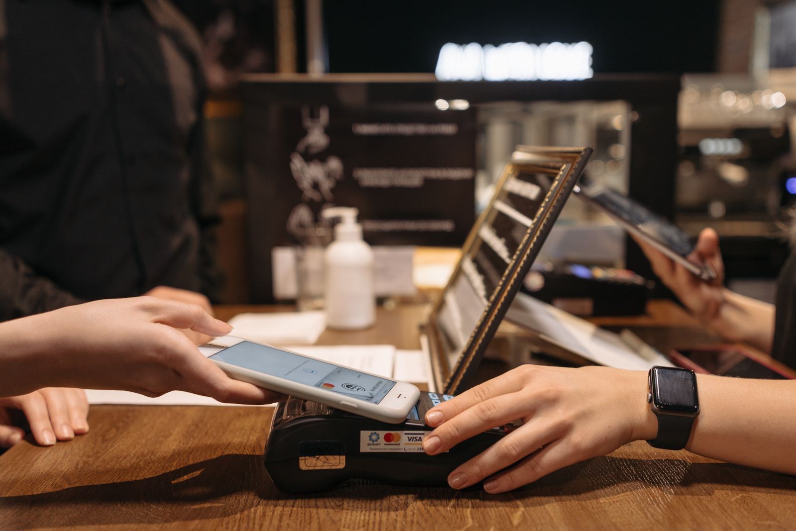 A customer holding a phone to a card terminal on a café counter to pay