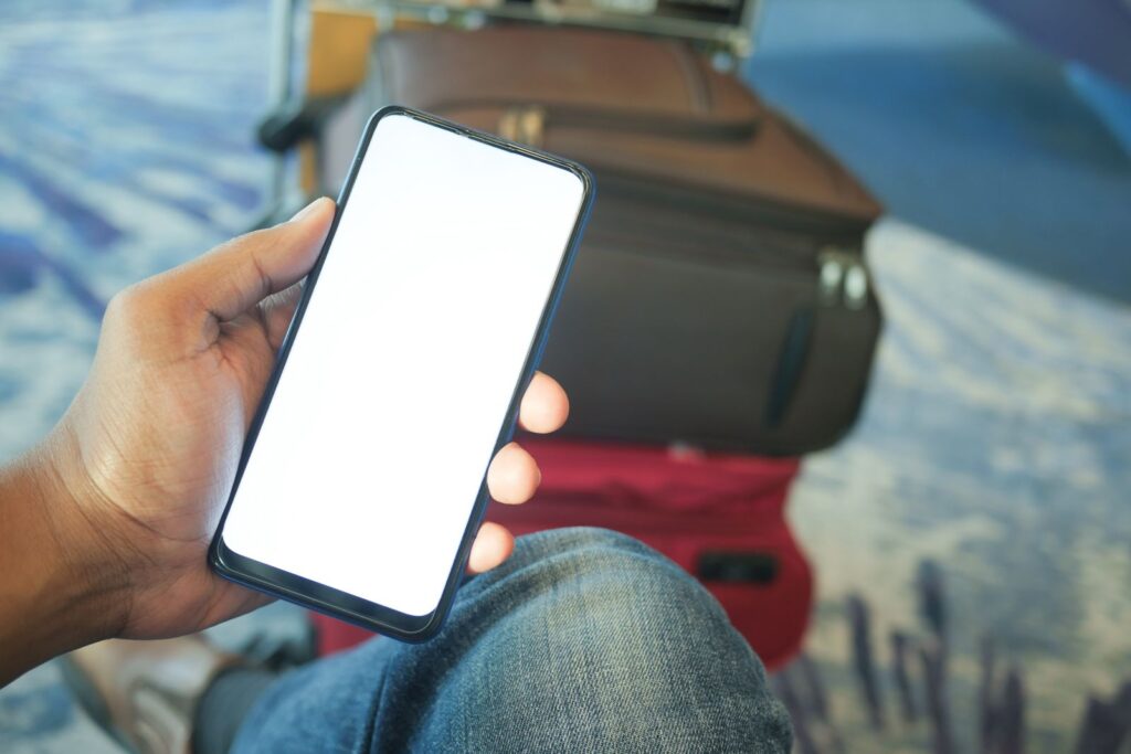 A hand holding a phone with a blank screen in an airport, luggage behind
