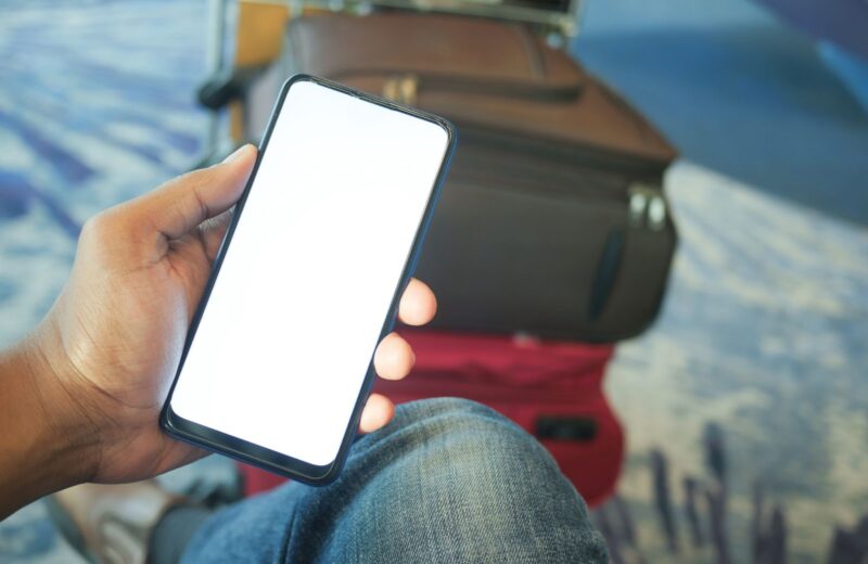 A hand holding a phone with a blank screen in an airport, luggage behind
