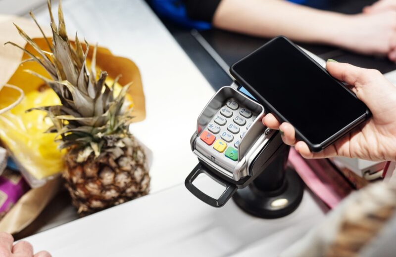 A hand holding a phone over a card terminal at a shop counter beside a pineapple