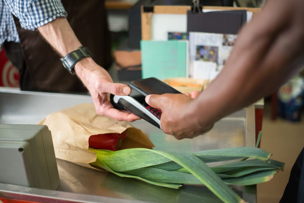 A shopper paying for groceries at a checkout with a phone held to the terminal