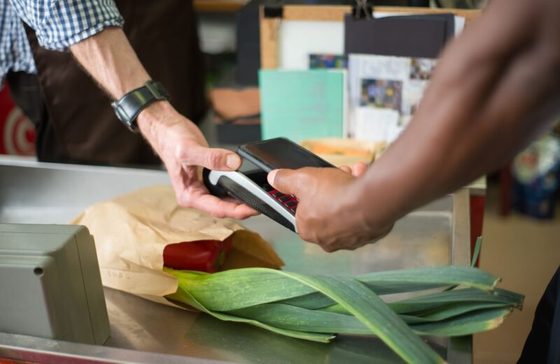 A shopper paying for groceries at a checkout with a phone held to the terminal