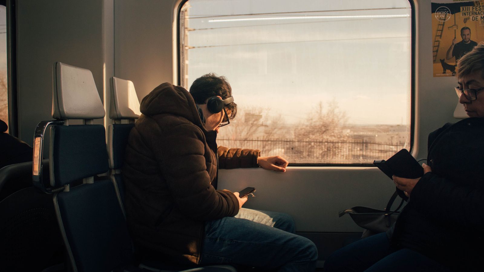 Passengers on a train by the window, one in headphones looking out at the countryside