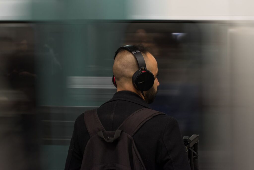 A man in headphones waiting on an underground platform, seen from behind