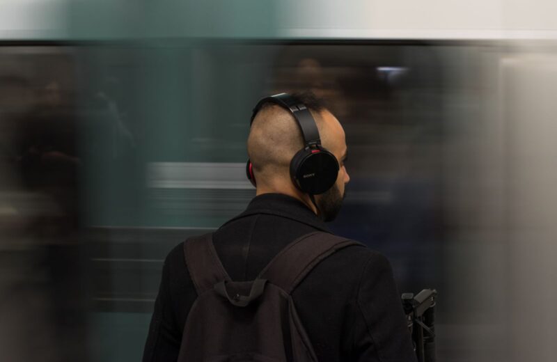 A man in headphones waiting on an underground platform, seen from behind