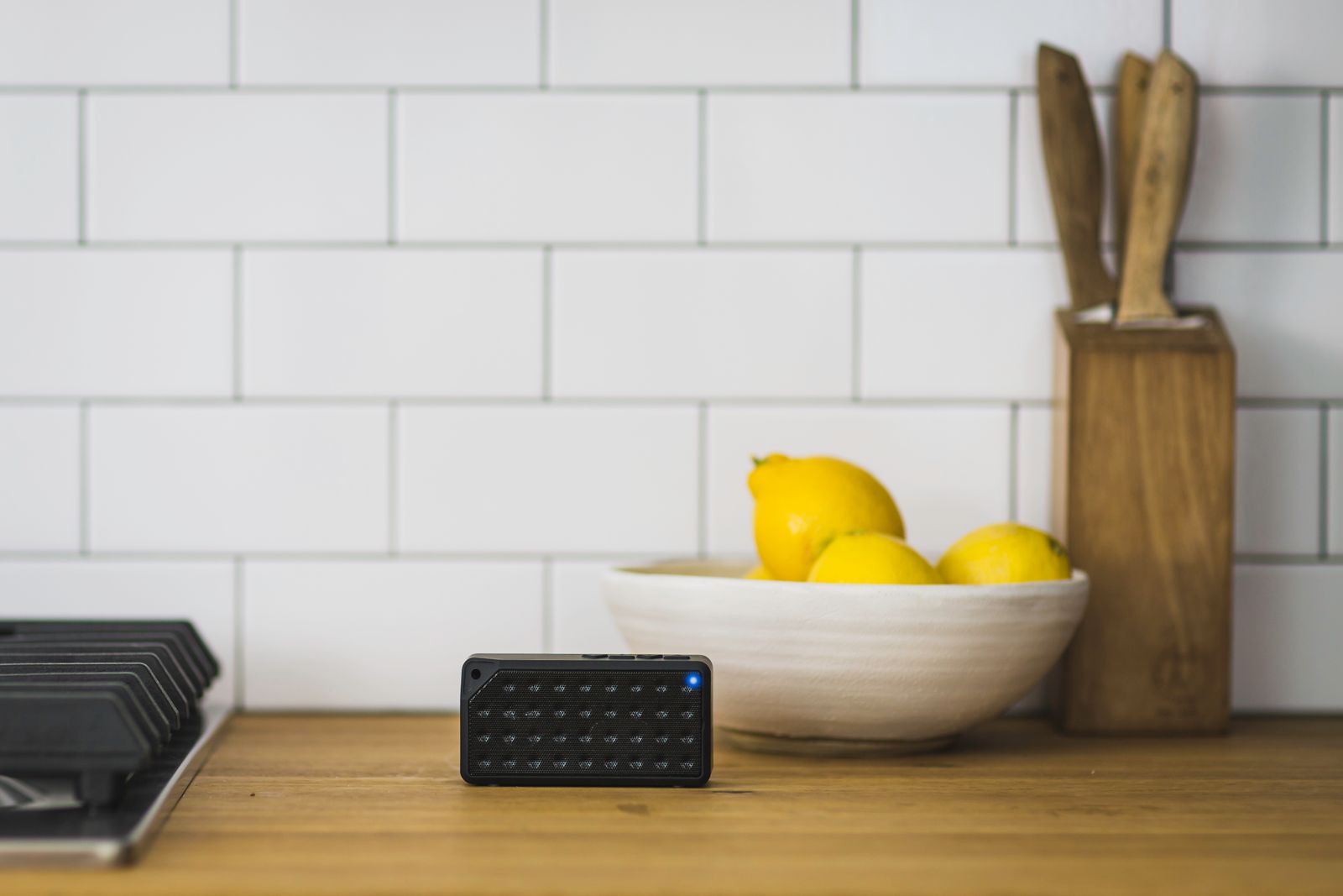 A small wireless speaker on a kitchen counter beside a bowl of lemons