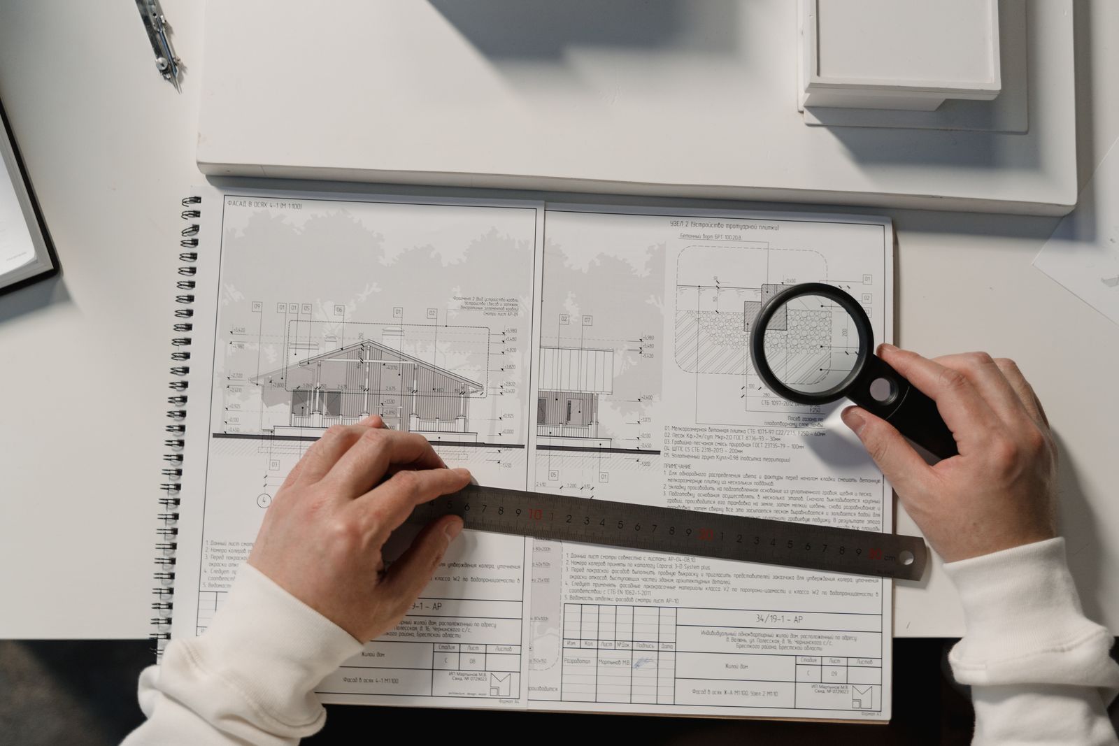 Hands with a ruler and a magnifying glass over printed floor plans