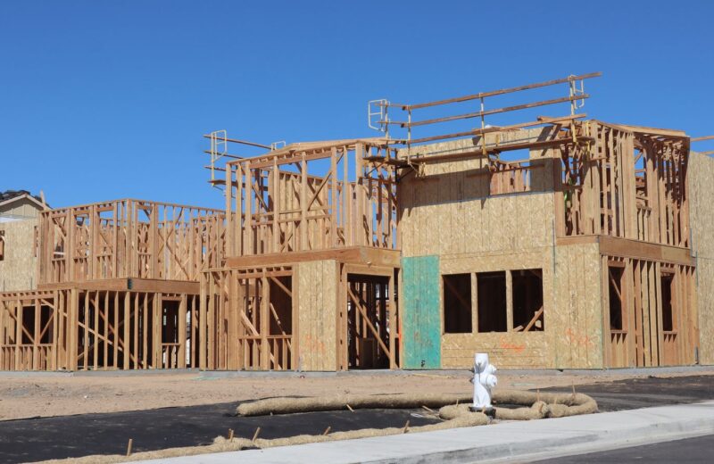 Timber-framed walls of new houses on a building site under a blue sky