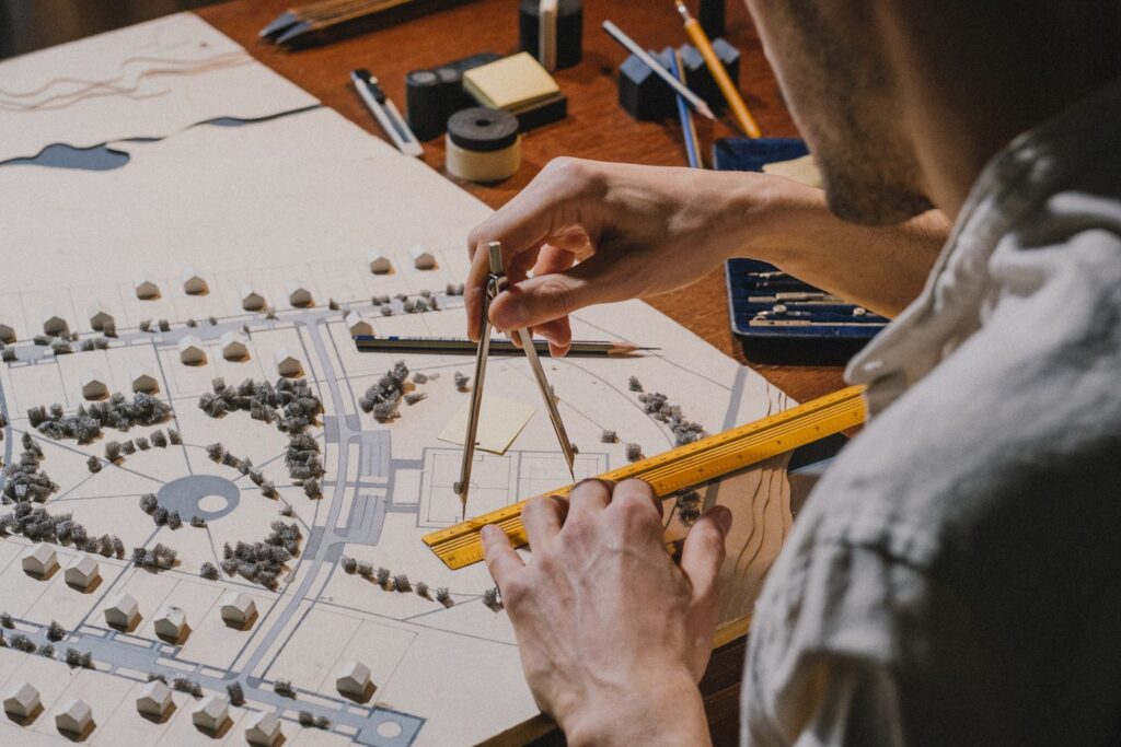 An architect using dividers and a ruler over a site model with paper trees