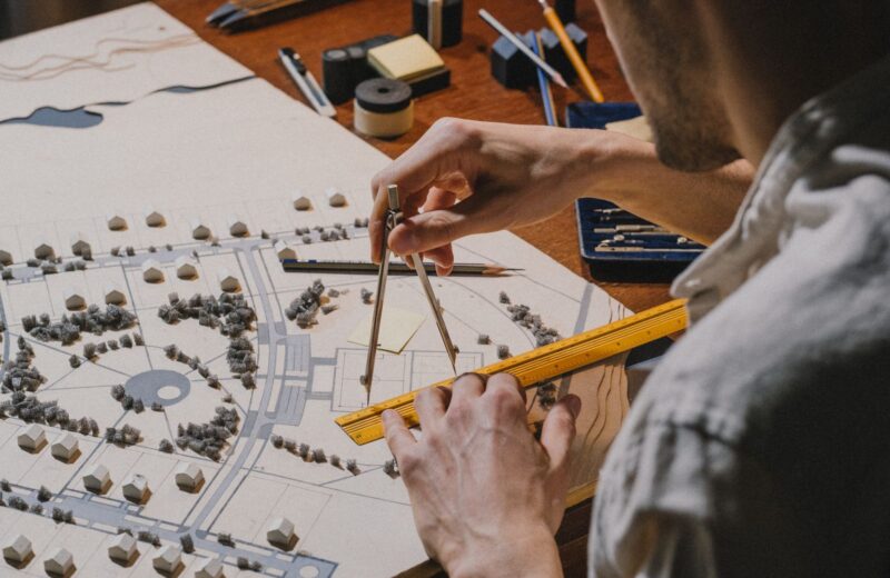 An architect using dividers and a ruler over a site model with paper trees