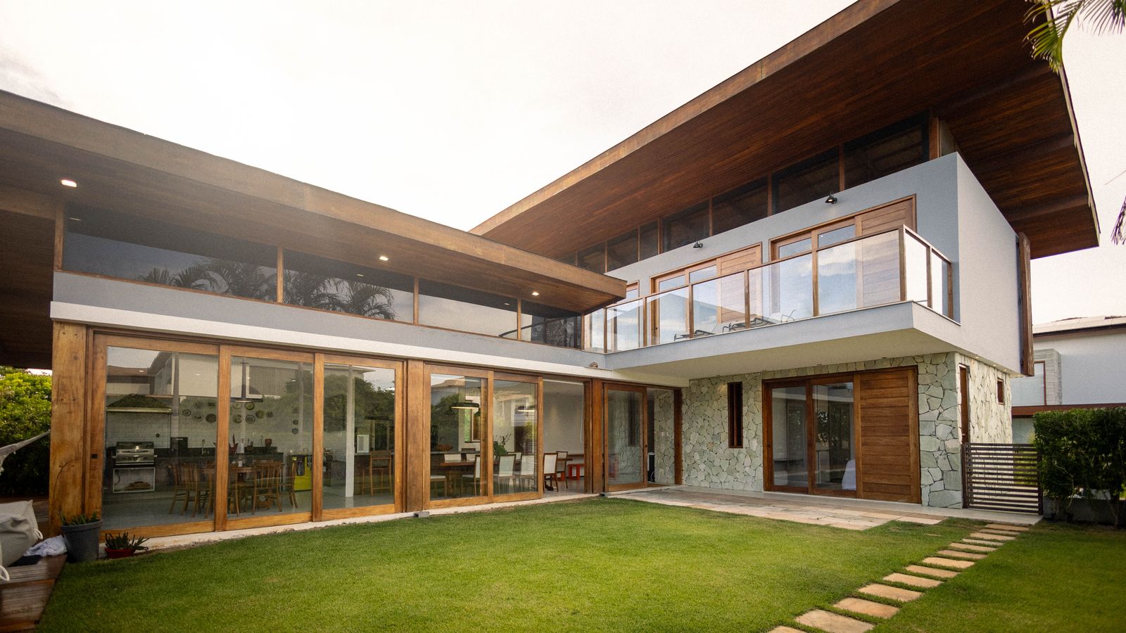 Single-storey house with timber soffits, full-height glazing and a lawn at dusk