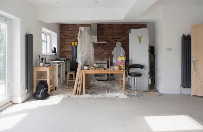 Open-plan room at fixing stage with plastered walls, a radiator and tools on the floor