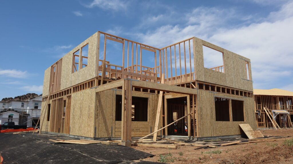 Two-storey timber frame of a new house with sheathed walls under a blue sky