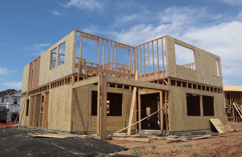Two-storey timber frame of a new house with sheathed walls under a blue sky