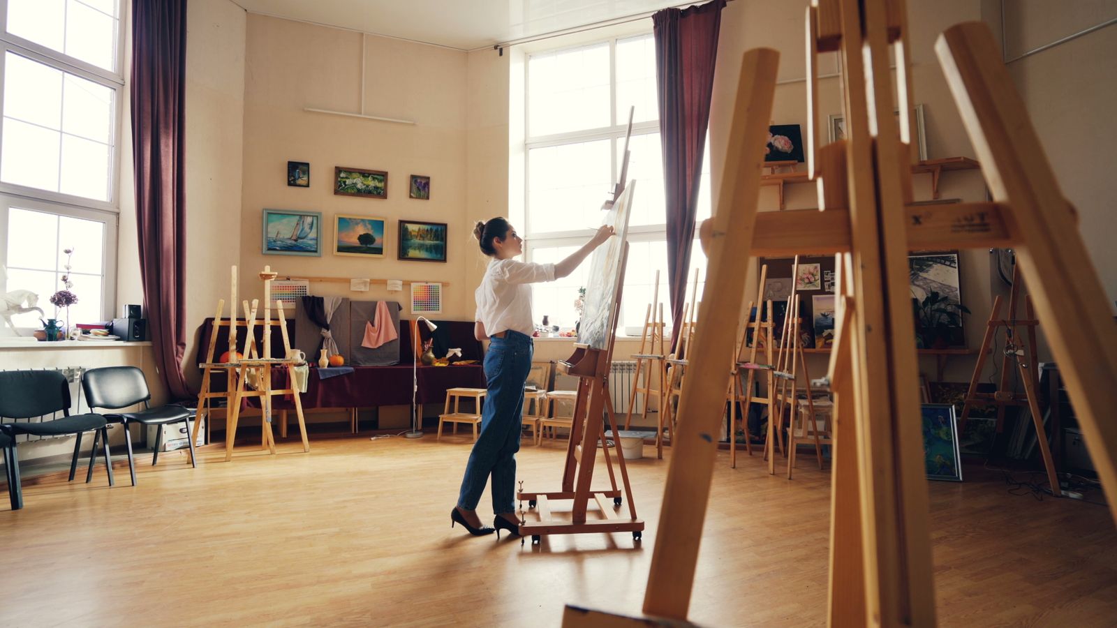 Painter working at an easel in a sunlit art room full of easels