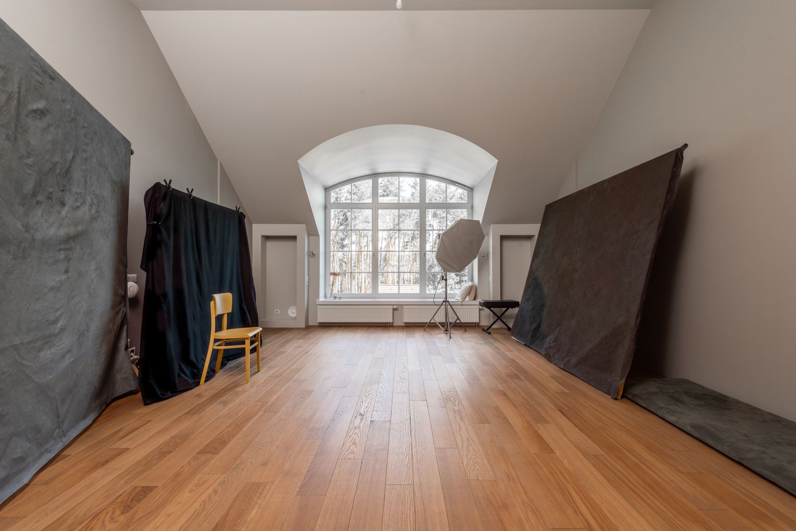Empty daylight studio with a sloping ceiling, tall window and wooden floor