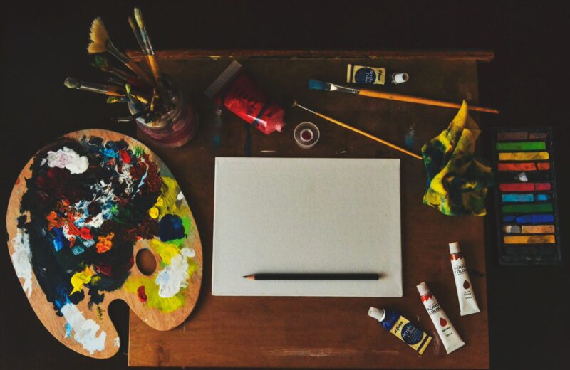 Brushes, paint tubes, a palette and a blank canvas on a work table