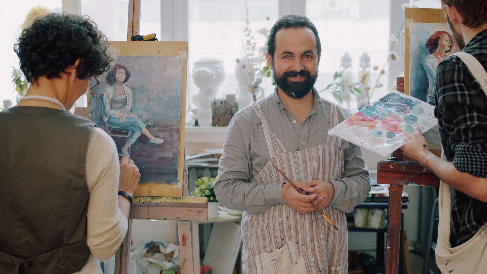 A tutor in a paint-spattered apron in front of students' easels