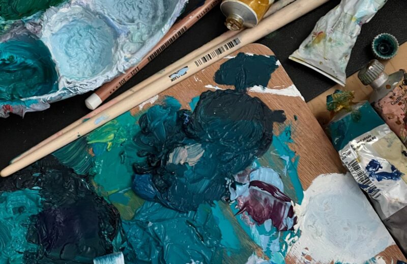 A well-used palette with teal and white oil paint, brushes and tubes