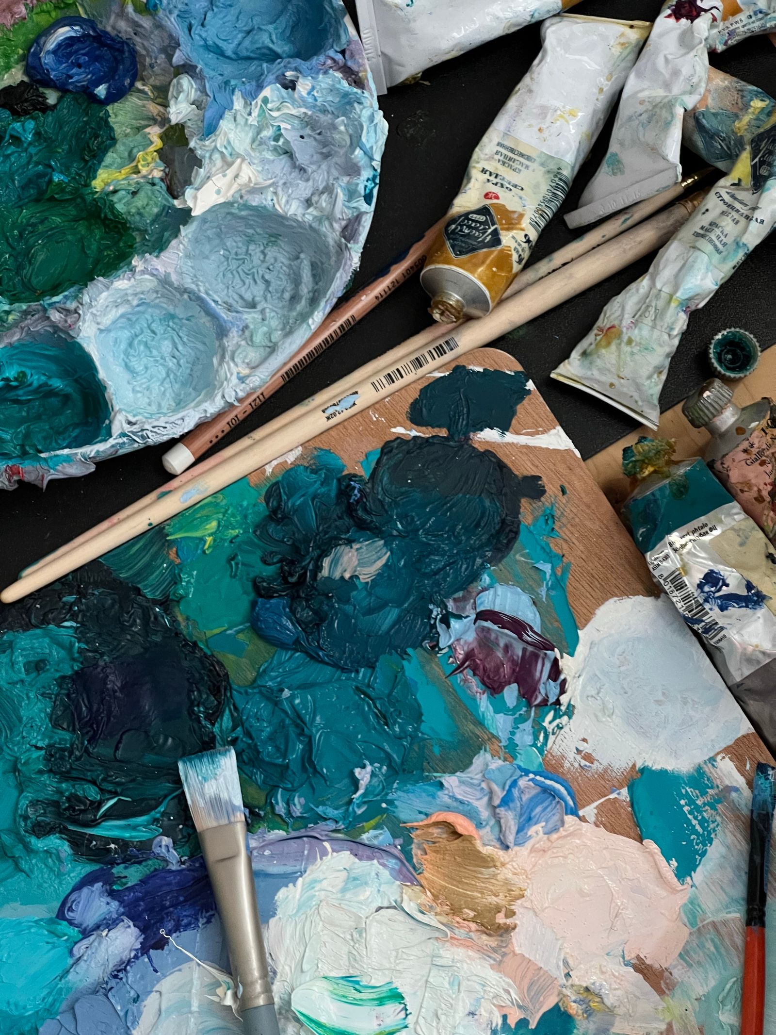 A well-used palette with teal and white oil paint, brushes and tubes