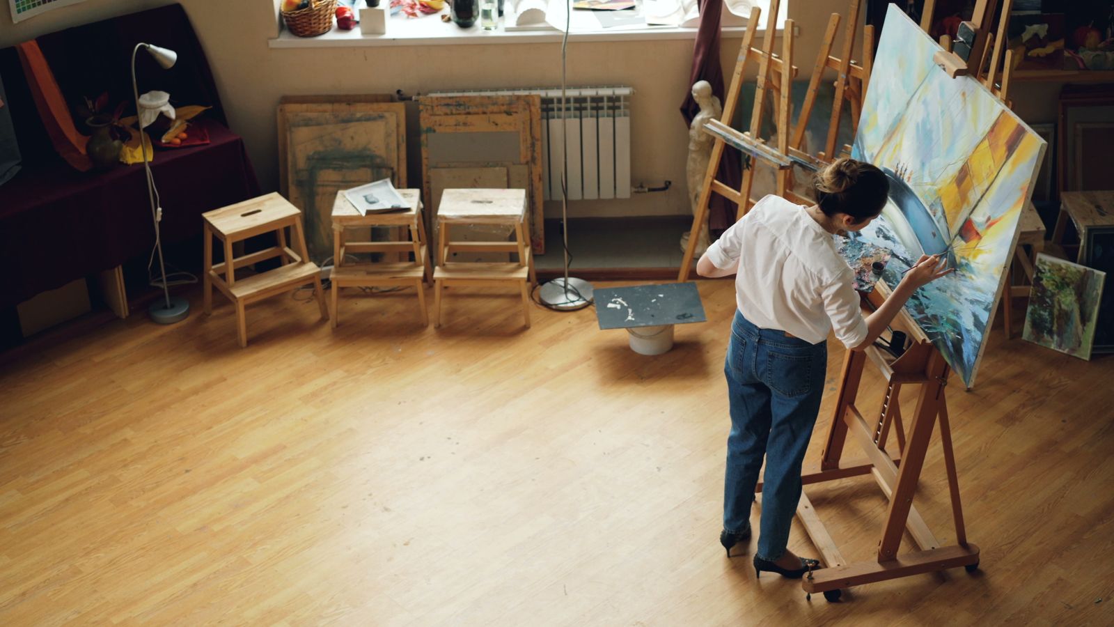 A painter seen from behind working on a large canvas in a bright studio