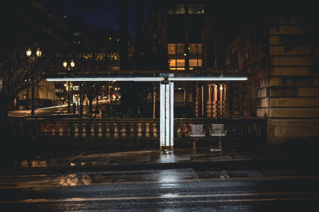 A lone bus stop lit by street lights on an empty street at night