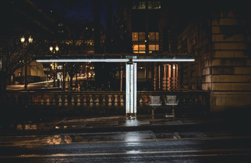 A lone bus stop lit by street lights on an empty street at night