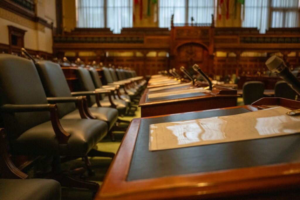 An empty council chamber with wooden desks and microphones