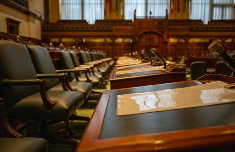 An empty council chamber with wooden desks and microphones