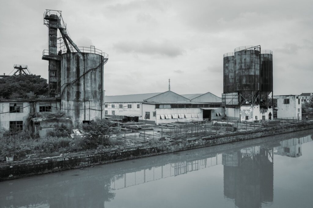 Black and white view of rusting silos beside a river