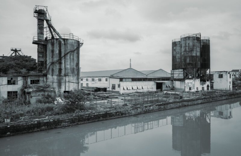 Black and white view of rusting silos beside a river