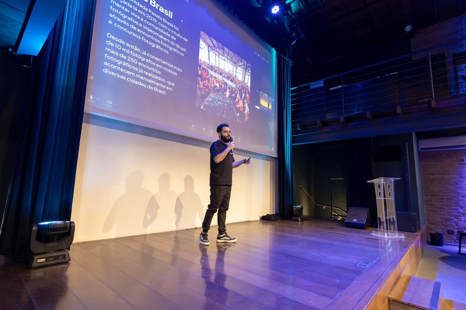 A speaker on a dark stage in front of a projected slide, seen from the audience
