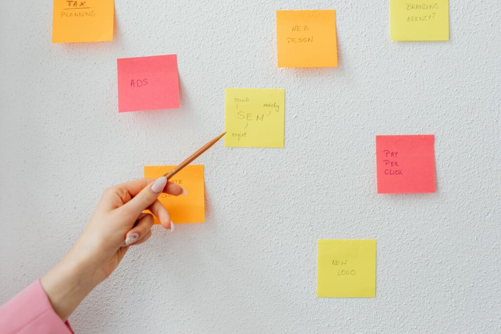 A hand pointing at coloured sticky notes on a white wall