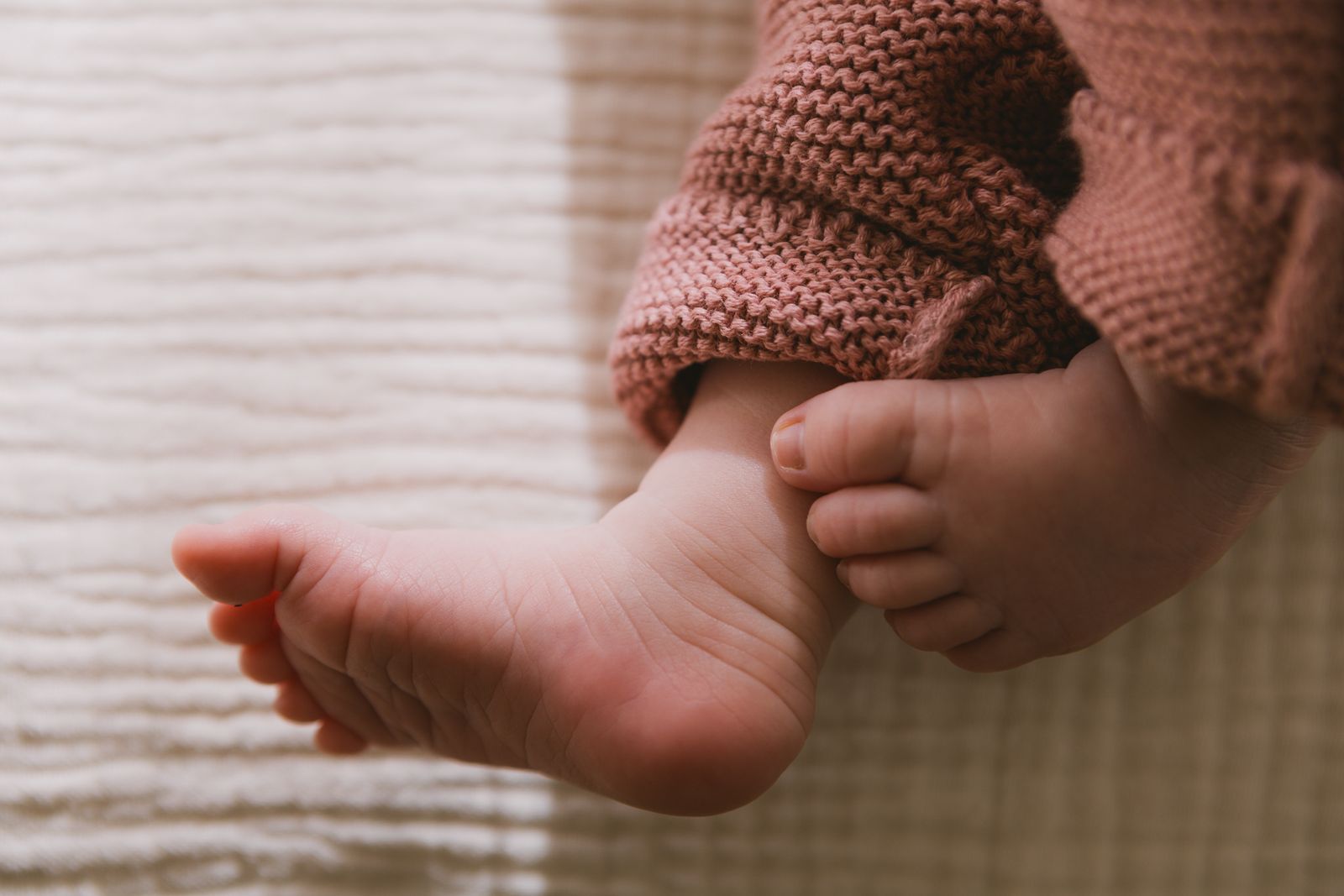 A baby's bare foot beside a knitted sleeve on a soft blanket