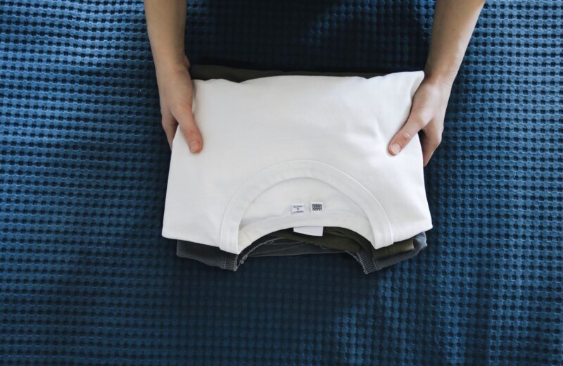 Hands folding a white cotton top on a blue bedspread