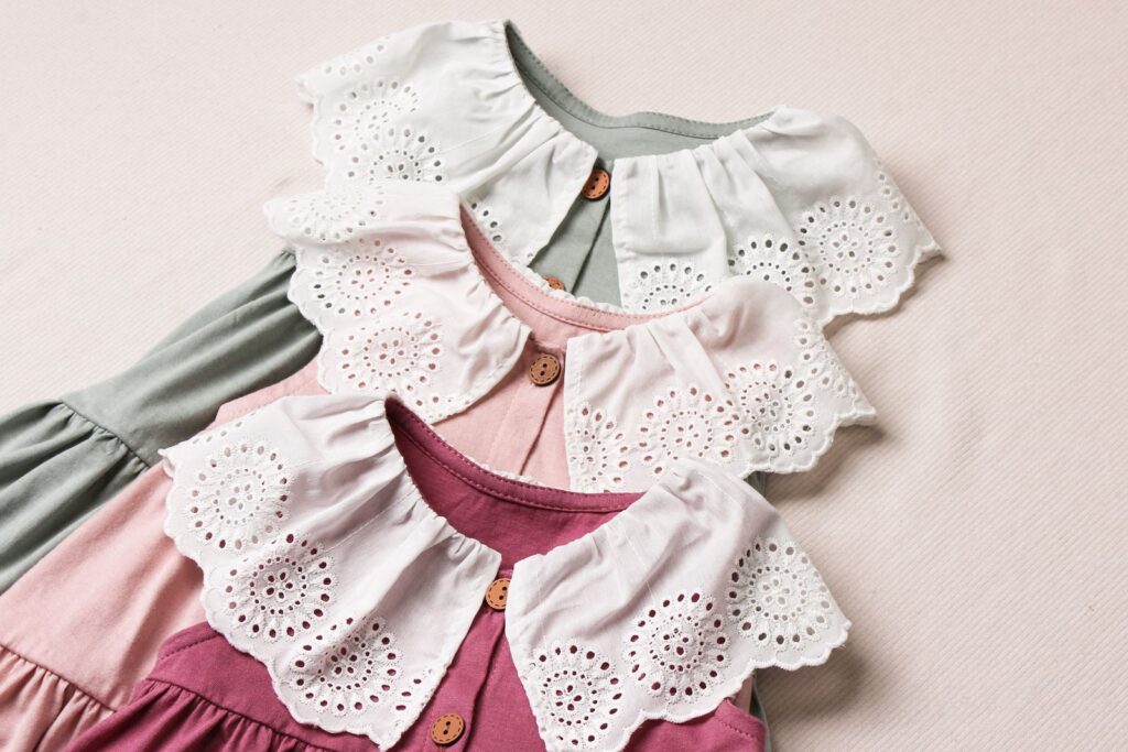 Three baby dresses with lace collars laid side by side