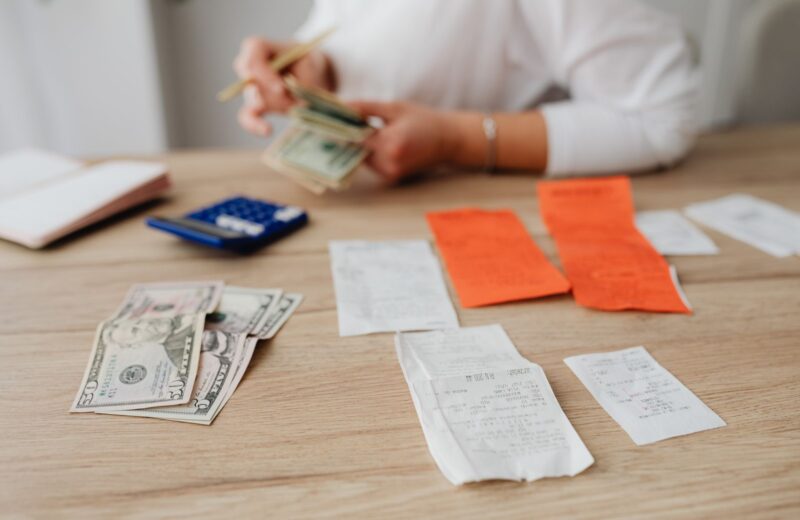 Hands counting cash beside receipts and a calculator on a wooden table