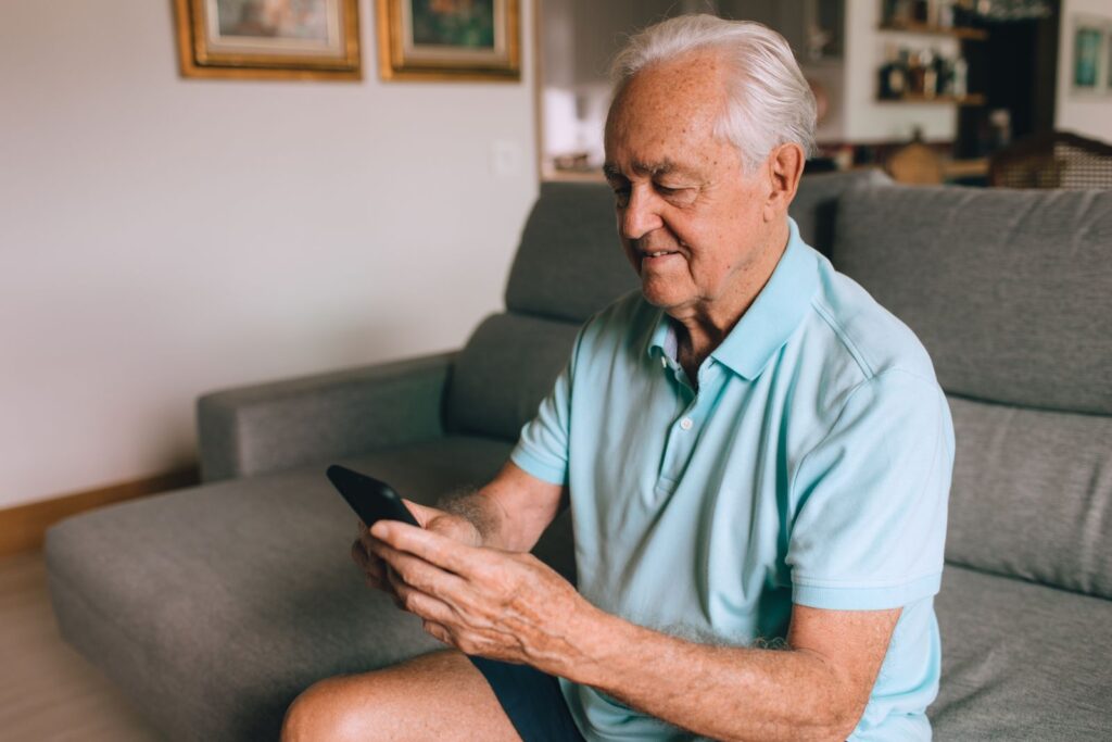An older man in a polo shirt reading a message on his phone at home