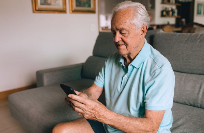 An older man in a polo shirt reading a message on his phone at home
