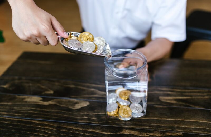 A hand dropping coins into a glass jar on a wooden table