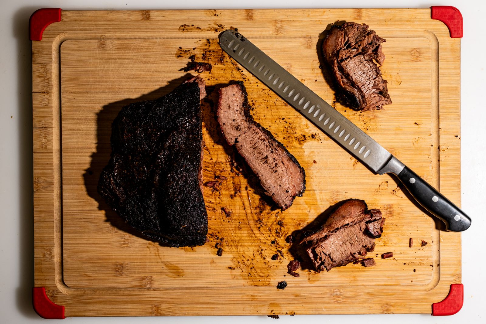 A smoked brisket, partly sliced, on a cutting board beside a long slicing knife