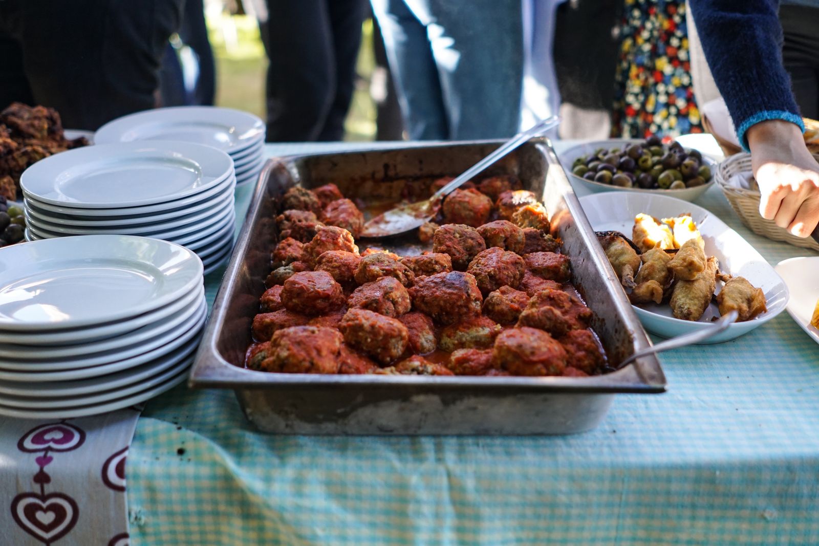 A buffet tray of meatballs in sauce beside a stack of plates at an outdoor party