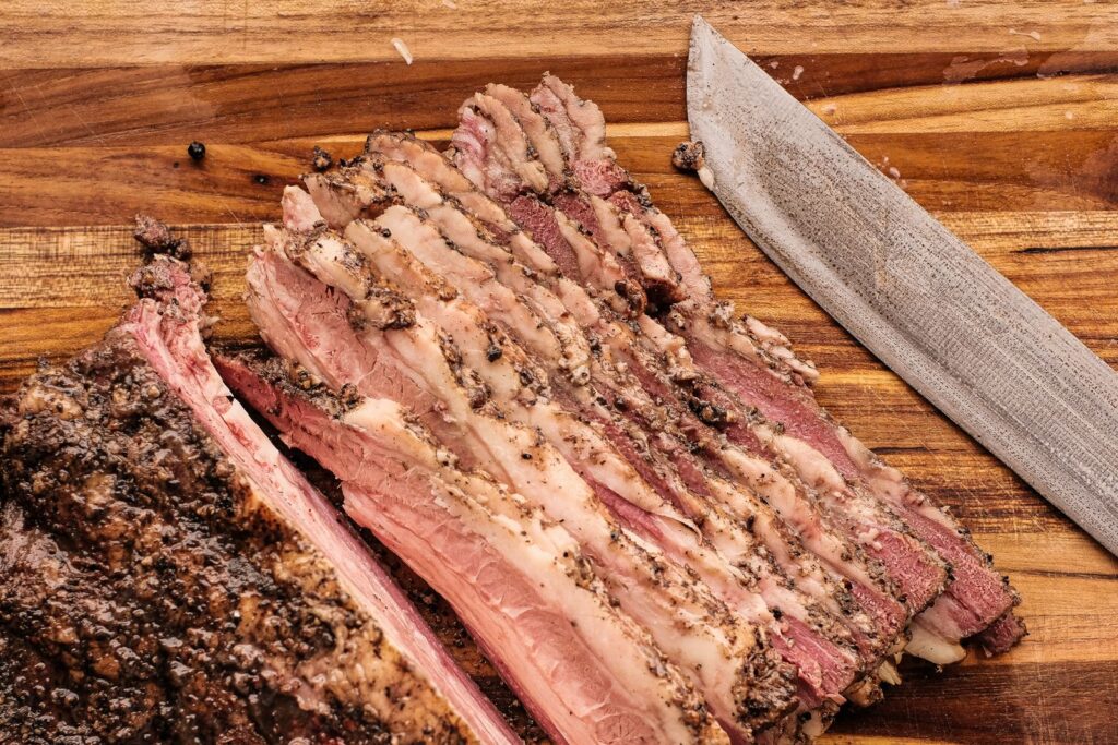 Slices of brisket fanned out on a wooden board next to a knife