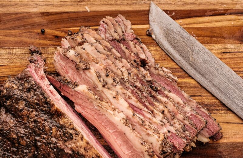 Slices of brisket fanned out on a wooden board next to a knife
