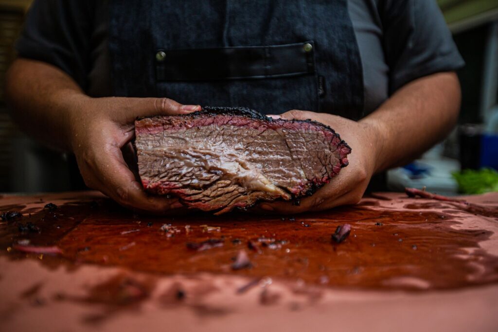 Hands holding a cooked brisket over a wooden board